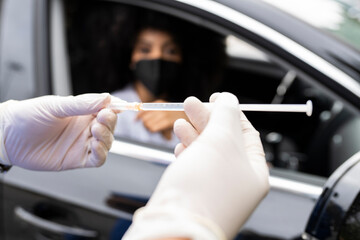 Cropped unrecognizable nurse in latex gloves and uniform preparing to vaccinate African American female patient inside the car on a drive through mobile clinic during coronavirus outbreak