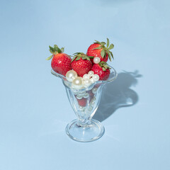 Creative concept with strawberries, white pearls  and glass jar on pastel blue background. Retro fruit or food layout. Romantic spring or summer idea.