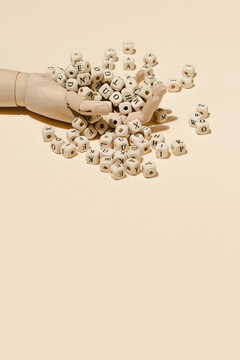From above of wooden hand with pile of alphabet letters on cubes scattered on beige background in studio