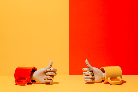 Creative ornamental wooden hand with thumbs up inside colorful mug on yellow and red background in studio