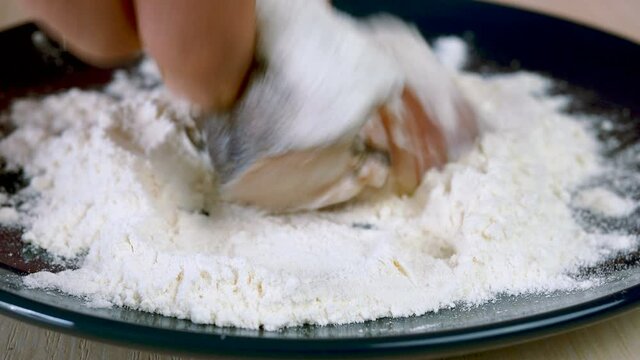 Chef dips slices of hake or pollock fish into flour in plate for preparation delicious fish dish. Fried fish recipe. Selective focus.