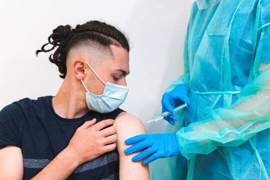 Crop female medical specialist in protective uniform, latex gloves and face mask vaccinating hispanic man patient in clinic during coronavirus outbreak
