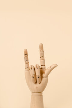 Creative wooden hand showing rock and roll gesture on beige background in studio