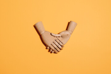 Top view of wooden hands demonstrating handshake as sign of agreement placed on yellow background