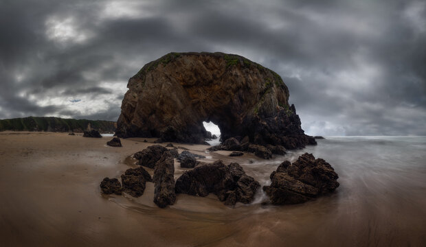 Majestic view of rough rocky formations on wet Penarronda beach under cloudy sky in Asturias