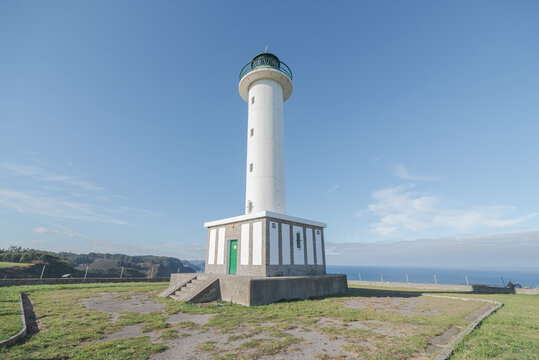 Asphalt road leading to white lighthouse placed in Faro de Lastres in Asturias in Spain under cloudless blue sky in daytime