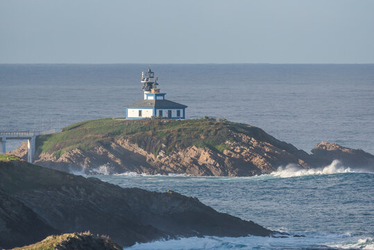 Spectacular scenery of bridge leading to rocky island covered with green grass with lighthouse placed in wavy ocean in Faro Illa Pancha in Galicia in Spain in daytime