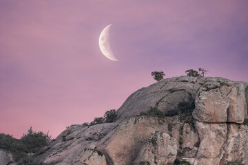Low angle of spectacular scenery of rough rocky mountain under pink sunset sky with waning moon in Sierra de Guadarrama National Park
