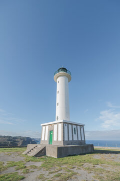 Asphalt road leading to white lighthouse placed in Faro de Lastres in Asturias in Spain under cloudless blue sky in daytime