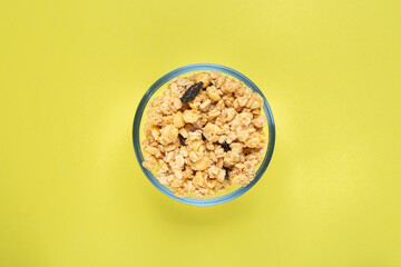 Healthy breakfast. Oatmeal with dried grapes in a glass bowl on a yellow background. Musli is healthy food. Space for text.