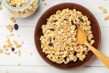 Healthy breakfast. Muesli with dried grapes in a clay bowl on a white wooden table. Muesli is scattered on the table. Space for text.