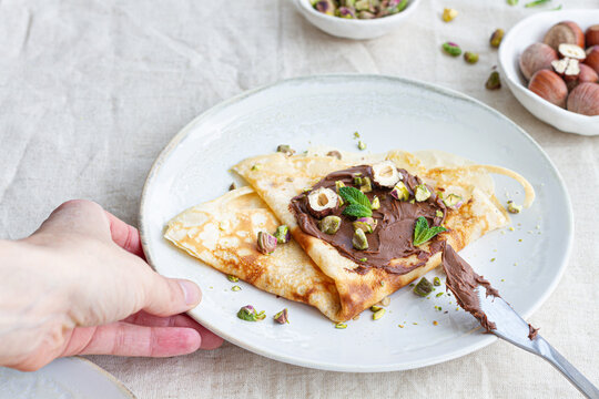 Cropped unrecognizable book holding plate with delicious crepes garnished with chocolate and nuts on table for breakfast