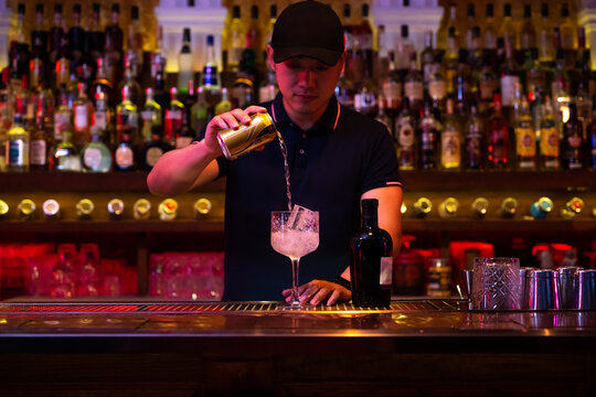 Young Asian bartender pouring tonic water to the glass for preparing a gin tonic cocktail in the bar