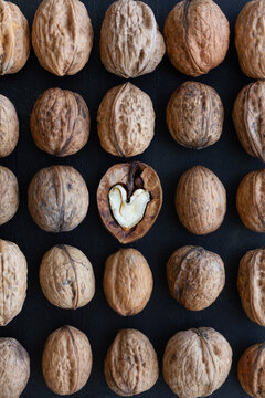 Top view of textured backdrop representing heart shaped walnut center among whole nuts with uneven nutshells