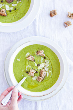 Top view of crop unrecognizable person sitting at table and eating appetizing zucchini cream soup for lunch