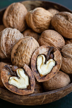 Round shaped wooden bowl full of crunchy walnuts with dry uneven nutshells on table