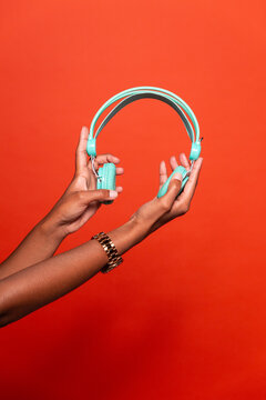 Crop anonymous African American female showing wireless headphones on outstretched hand against red background in studio