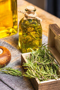 Glass bottle of essential oil with rosemary twigs and burning organic wooden candle on gray table