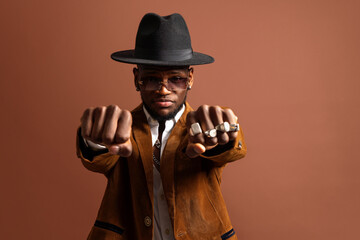 Young ethnic male in hat and stylish wear looking at camera on brown background