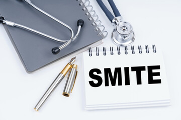 On the table are a stethoscope, a pen and a notebook with the inscription - Smite