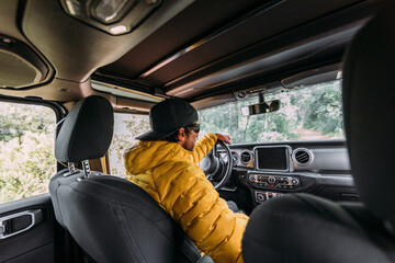 From behind inside view of a driver wearing a cap and sunglasses in an off-road car looking away