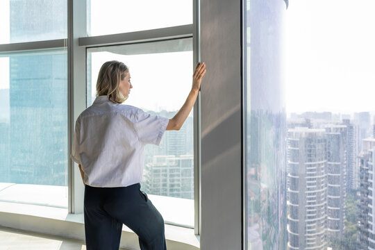 Back view of lonely girl in empty office watching the city from big window