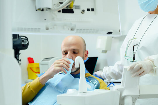 Crop unrecognizable female dentist in uniform and sterile mask against man pouring water from tap into glass after oral operation