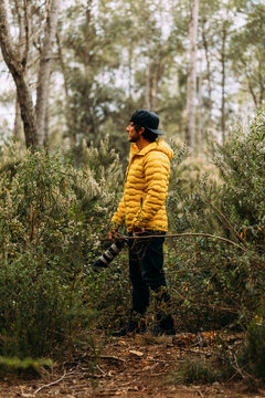 Fototapeta Side view of a photographer in a cap and yellow jacket on the mountain looking away