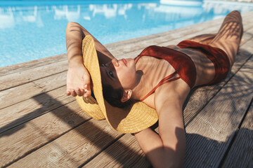 Beautiful woman in hat relaxing on wooden pier under palm leaves at pool, enjoying summer vacation....