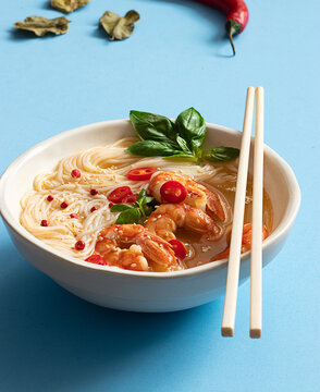 Tom yum soup in bowl with chopsticks on blue background