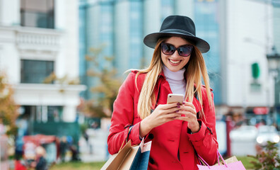 Smiling woman using mobile phone during the shopping in the city. Consumerism, lifestyle concept