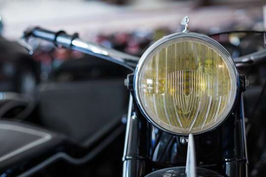 Closeup of yellow headlight of old fashioned motorbike placed against blurred background of workshop