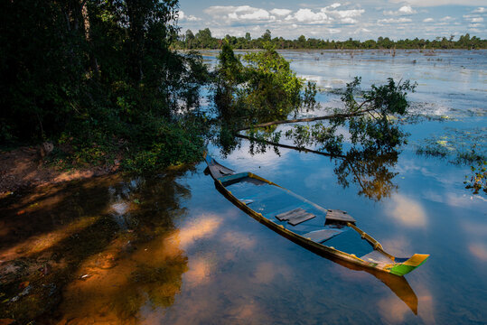 Aged damaged boat on river with pure water and fallen trees in Cambodia on summer day