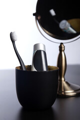 A black toothbrush and a toothpaste in a black glass. The glass is reflected in the mirror.