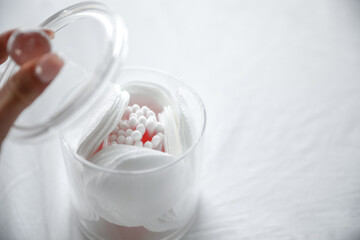 A hand opening clear container for cotton pads on a white background. 