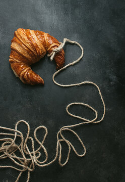 From above of delicious freshly baked traditional croissant wrapped with rope on black background