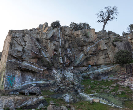 Drone view of man hanging on rope while painting graffiti on steep stony slope