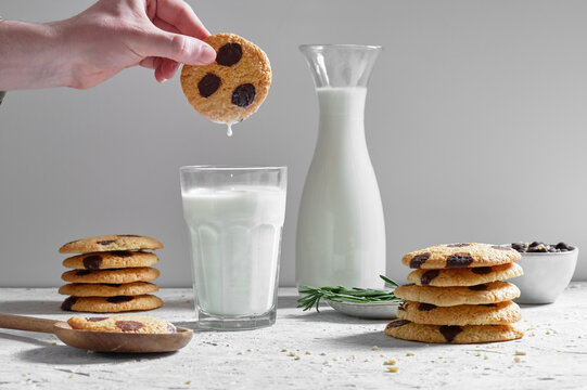Crop anonymous person dipping delicious sweet homemade cookies with chocolate chips into glass of fresh milk