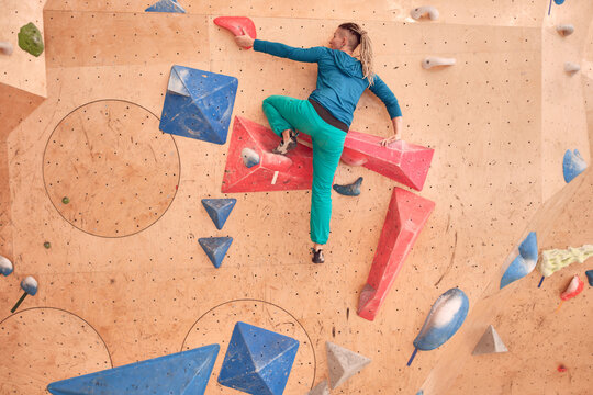 Female athlete climbing artificial wall during bouldering workout in professional gym