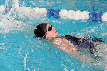 teenage girl swimming in swim meet doing backstroke