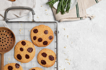 Top view of freshly baked sweet cookies with chocolate chips on metal grid placed on table with various kitchen tools and green rosemary branches