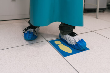 Crop anonymous chemist or doctor wearing long apron and medical overshoes standing on step floor sign in modern hospital