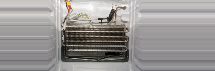 Disassembled white modern home freezer with stainless steel radiator, copper piping and sensor,...