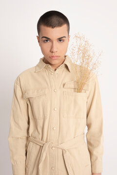 Androgynous male model in trendy shirt and with bunch of dried plants looking at camera on white background in studio