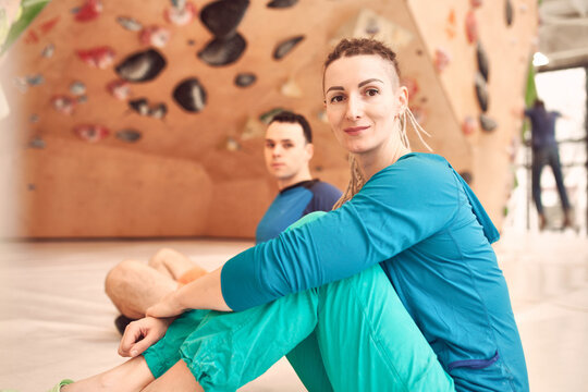 Side view of female and male climbers sitting on floor near artificial wall in contemporary bouldering center while looking at camera