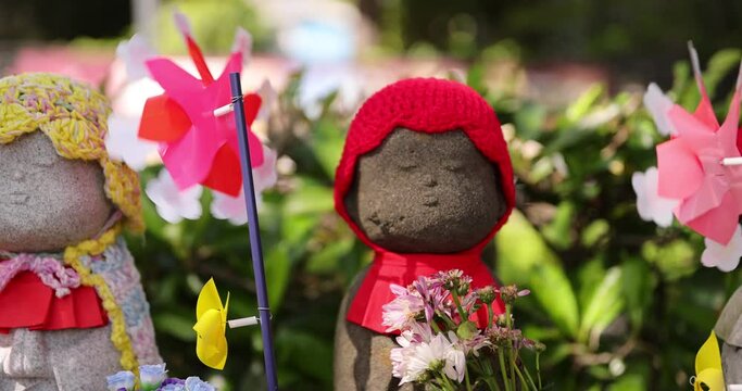 A slow motion of moving colorful windmills with Jizo statue daytime closeup
