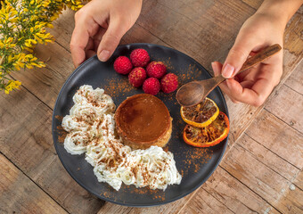 From above of crop anonymous cook with plate of yummy baked flan with ripe raspberries and cinnamon powder