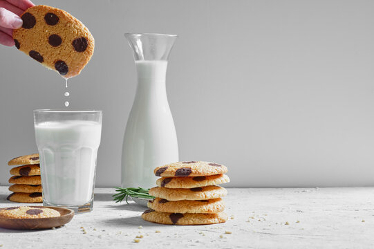 Crop anonymous person dipping delicious sweet homemade cookies with chocolate chips into glass of fresh milk