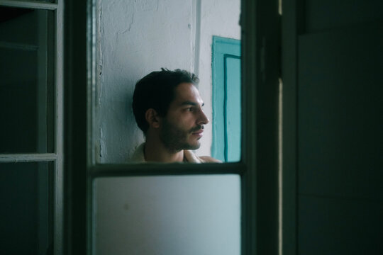 Calm shirtless male with beard leaning on shabby wall at home and looking away