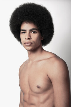 Young confident black man with six pack abs and Afro hairstyle looking at camera on white background